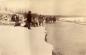 Large group of men lifting and carrying loaded sleds across the Chilkat river.